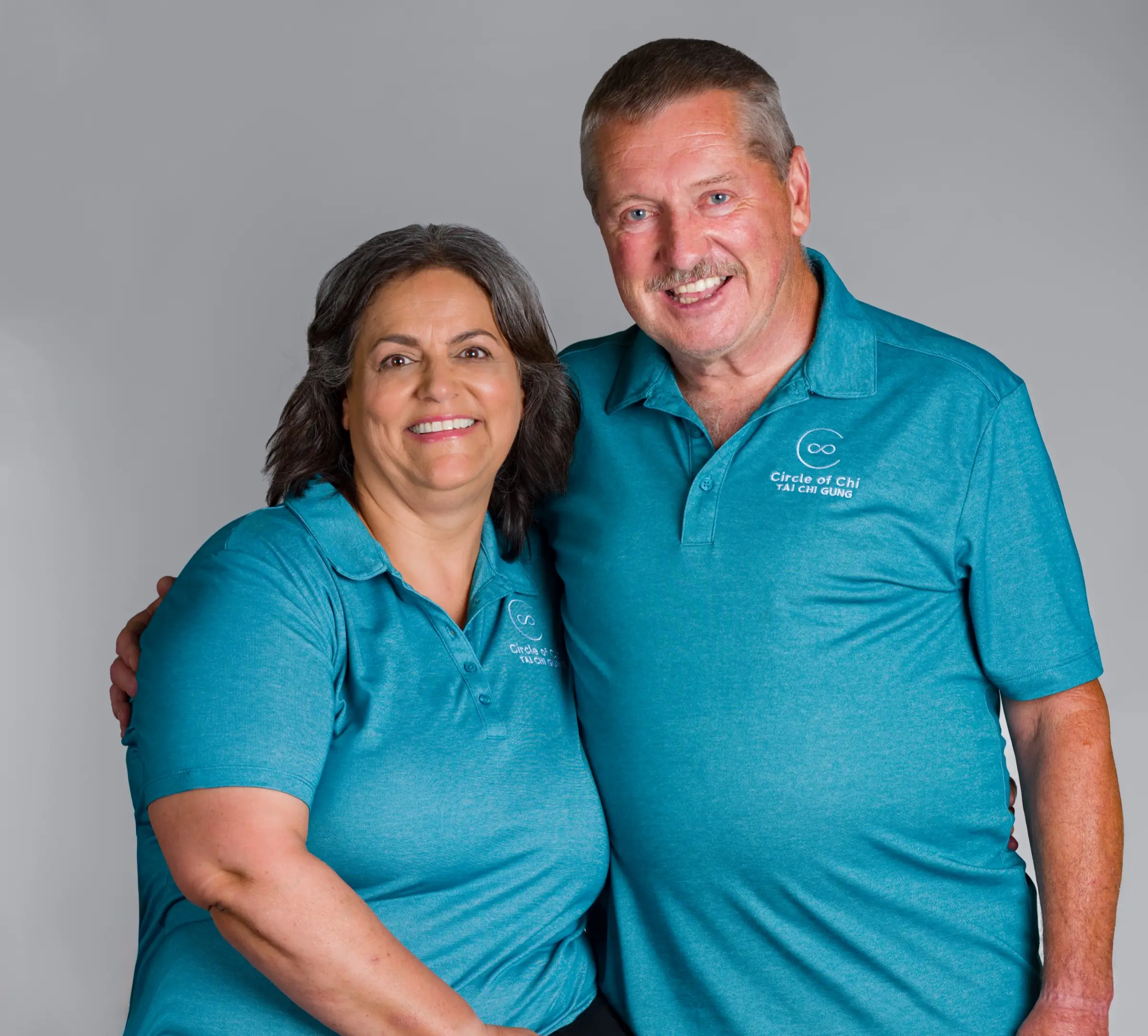 Esmeralda Reynolds arm in arm with a fellow practitioner, both wearing matching teal Circle of Chi polo shirts